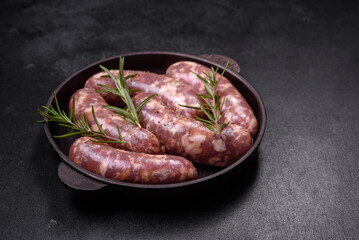 Raw pork sausages grill with spices and herbs on a dark concrete table