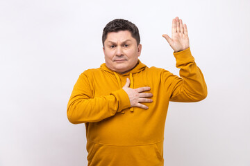 Honest sincere man giving promise with hand on heart, pledging allegiance, giving vow with responsible serious face, wearing urban style hoodie. Indoor studio shot isolated on white background.