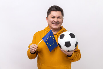 Satisfied middle aged man holds in hands flag of europe union and football ball, supporting...