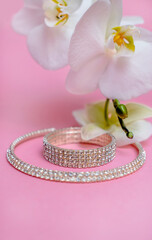 Bracelet and necklace and white orchid on pink background
