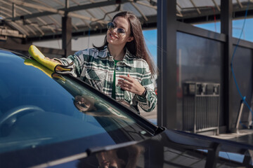 A young female cleaning and polishing her car with yellow microfiber cloth. Concept of car taking care