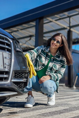 A young female cleaning and polishing her car with yellow microfiber cloth. Concept of car taking care