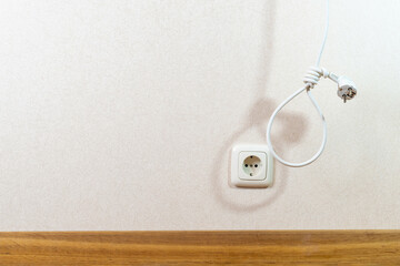 Electrical wire with plug as a hangmans knot on wall and socket background. Concept of energy...