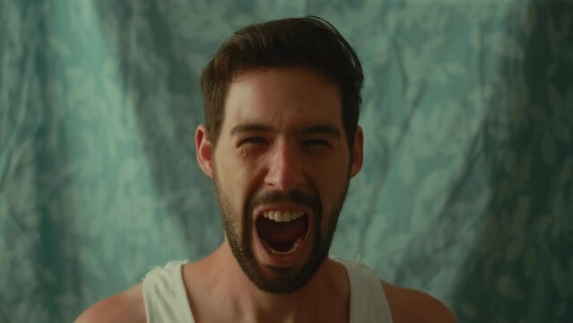 Young Caucasian male wearing a white undershirt yelling in front of the camera