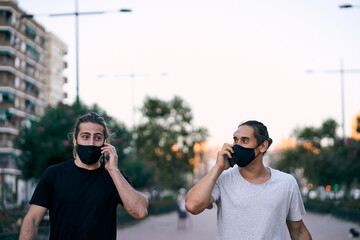 two caucasian young men walking on the city boulevard with face mask talking on the smartphone
