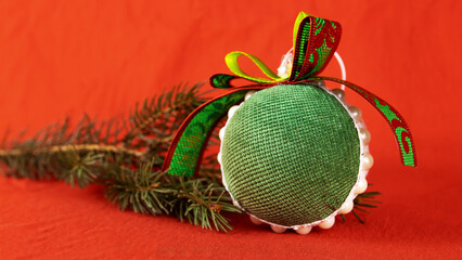 green round New Year's toy near a fir branch. the toy is made of fabric by hand
