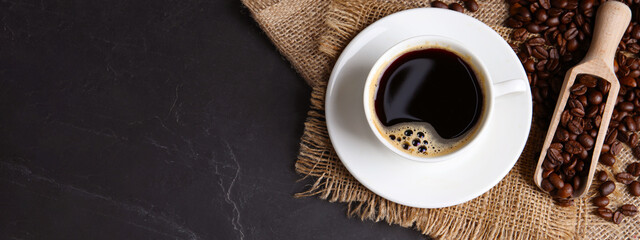 Cup of hot aromatic coffee and scoop with roasted beans on black table, top view with space for text. Banner design