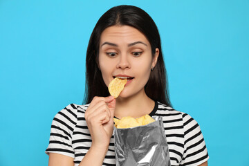 Beautiful woman eating potato chips on light blue background