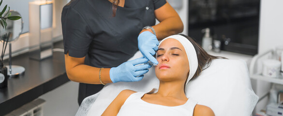 Wide indoor shot of caucasian licensed healthcare professional performing lip dermal filler on her beautiful caucasian female patient. Modern way to increasing fullness of lips. High quality photo