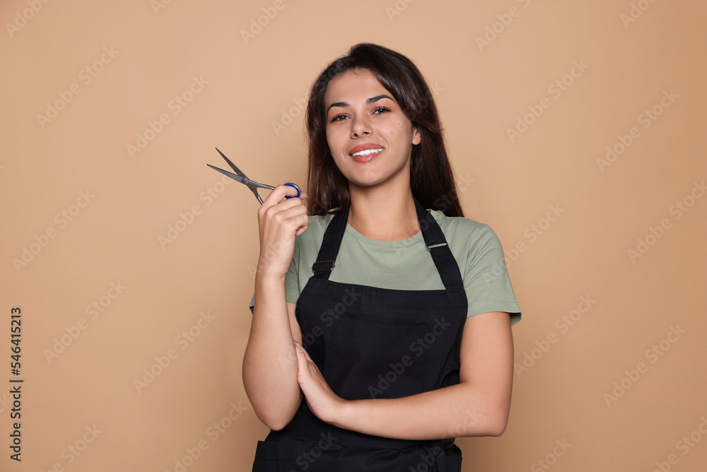 Wall mural Portrait of happy hairdresser with professional scissors against pale orange background