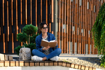 Young woman reading book on bench outdoors