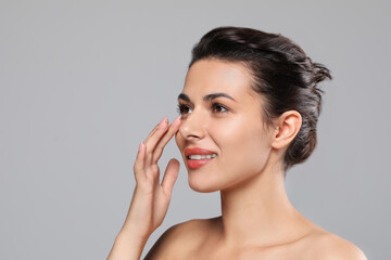 Woman applying cream under eyes on grey background, space for text. Skin care