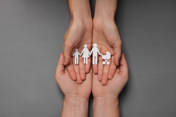 Couple holding paper family figures on grey background, top view. Insurance concept