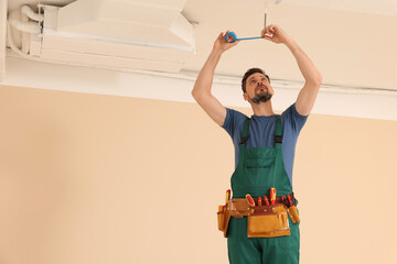 Electrician in uniform with insulating tape repairing ceiling wiring indoors. Space for text