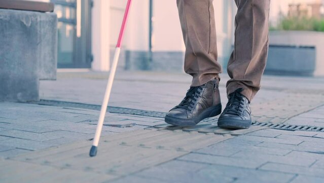 Blind person using white cane on straight tactile tiles to navigate road