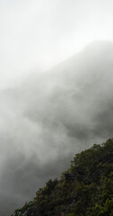 Thick fog hanging over dark mountainside. Vertical banner with clouds. Copy space background. 
