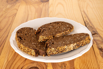 Three pieces of rye multigrain bread with a ceramic white plate on a wooden table, macro.
