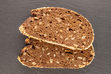 Two pieces of rye multigrain bread on slate stone, macro, top view.