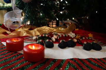 Burning candles on Christmas decorations at the foot of a Christmas tree decorated with spheres