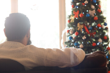 Man contemplating the decorated christmas tree by the window