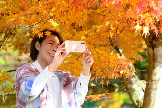 秋の季節を自撮りをしたり風景を撮影する女性 　右にコピースペースあり