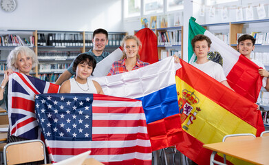 Group of young teenagers people holding international flags of many countries while studying in...