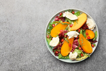 Delicious persimmon salad with cheese and pomegranate on grey table, top view. Space for text