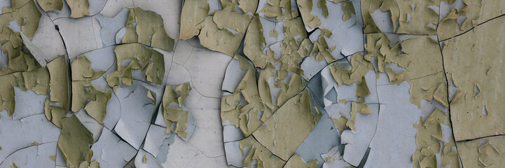 Peeling paint on the wall. Panorama of a concrete wall with old cracked flaking paint. Weathered rough painted surface with patterns of cracks and peeling. Wide panoramic grunge texture for background