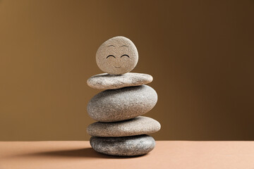 Fototapeta na wymiar Stack of stones with drawn happy face on table against dark beige background. Zen concept