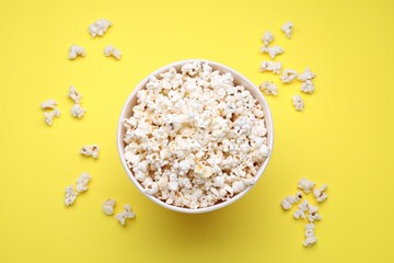 Paper bucket with delicious popcorn on yellow background, flat lay