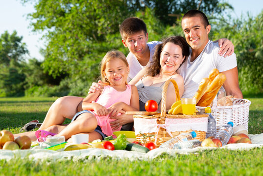 Happy parents with two kids having picnic together on green meadow in park. High quality photo