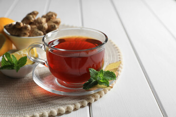 Cup of delicious ginger tea and ingredients on white wooden table