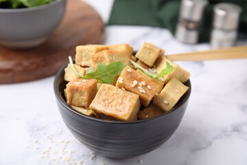 Delicious fried tofu with basil and sesame seeds in bowl on white marble table