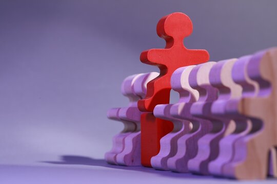 Wooden figures with red one on purple background, closeup and space for text. Recruiter searching employee