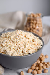 Chickpea flour in bowl and seeds on table, closeup
