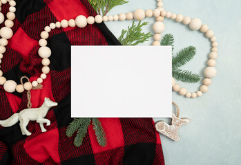 Holiday blank stationery card flat lay with red plaid fabric, spruce and fir sprigs, ornaments, and...