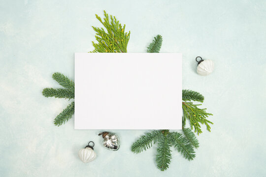 White blank holiday greeting card flat lay template with green spruce branches and small ornaments