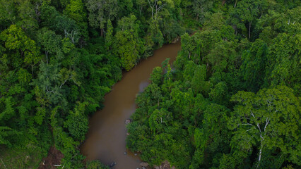Aerial view of countryside river passing through the green forest and mountain in Thailand.