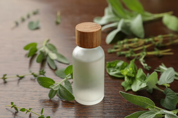 Bottle of essential oil and fresh herbs on wooden table