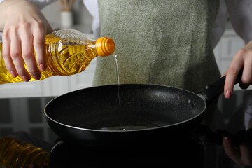 Woman pouring cooking oil from bottle into frying pan on stove, closeup