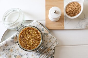 Jar and spoon of whole grain mustard on white wooden table, flat lay. Space for text