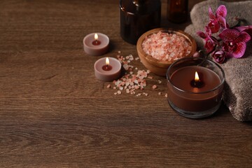Beautiful spa composition with burning candles, sea salt and flowers on wooden table. Space for text