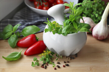 Mortar with fresh herbs near garlic, pepper and cherry tomatoes on wooden table, closeup