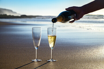 Pouring of cava or champagne sparkling wine on white sandy ocean beach on sunset in sunlights