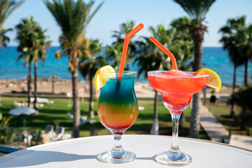 Colourful cold cocktails drinks served in glasses at outdoor cafe overlooking blue sea and palm trees, relax and holidays at sea