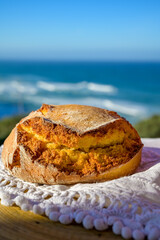 Portugeese homemade oven baked yellow corn bread served outdoor with view on blue Atlantic ocean in Lisbon area, Portugal