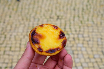 Hand with Portugal's traditional sweet dessert Pastel de nata egg custard tart pastry and view on...