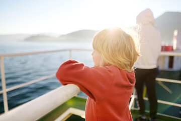 Blond little child is traveling with family by ferry or ship. Schoolboy is admiring the landscape...