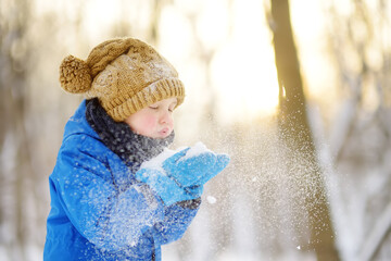 Little boy blowing snow from his hands. Child enjoy walking in the park on snowy day. Baby having...