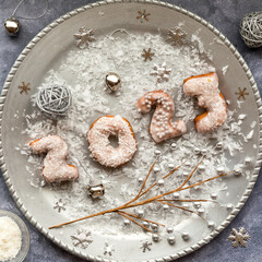 A silver platter with 2023 New Year donuts surrounded by festive decorations.